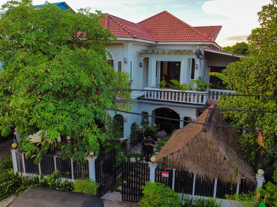 The house from above at sunset: red tile roof, the front balcony, the garden and the thatched sala behind the gate